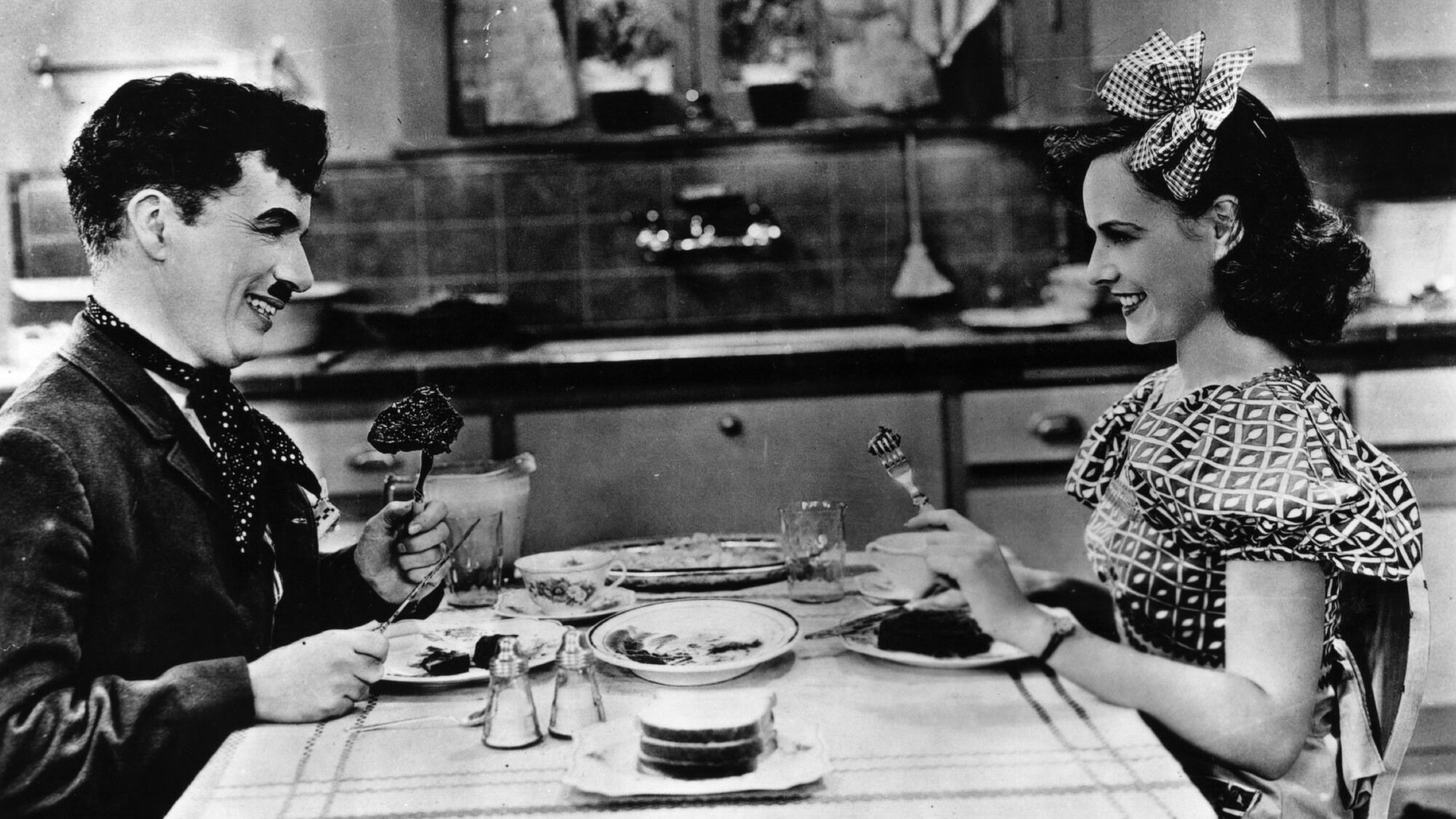 Charlie Chaplin smiles in a dinner scene in 