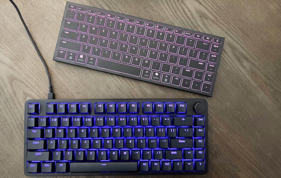 The Razer Joro and Sony Inzone KBD-H75 gaming keyboards rest on a brown wooden table with their RGB lighting activated.